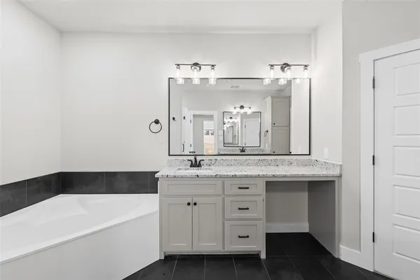 a bathroom with a granite countertop sink a bathtub a mirror and vanity