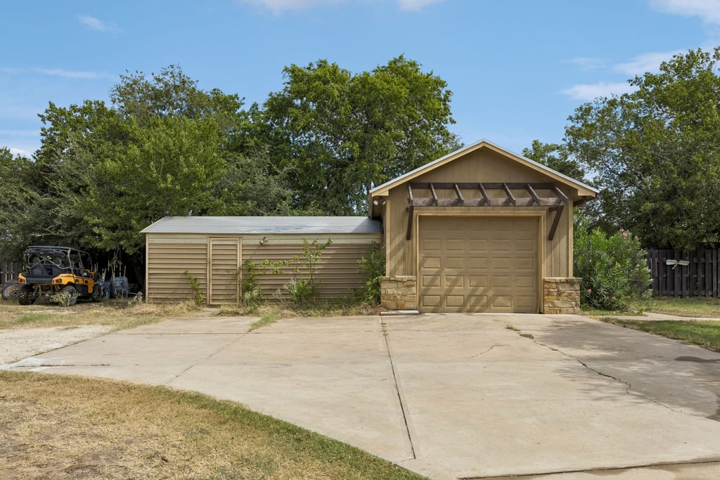 10111 Signal Hill Road Austin, TX 78737 - Photo 32 of 40 A spacious concrete driveway leads to a detached garage and storage building flanked by mature trees.