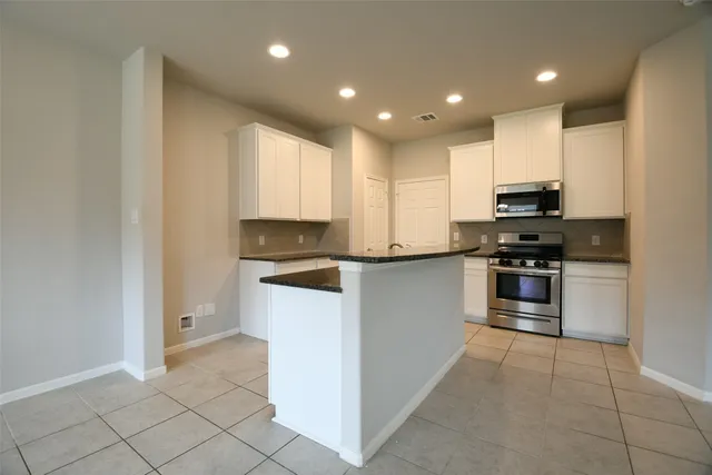 a kitchen with kitchen island granite countertop white cabinets and stainless steel appliances