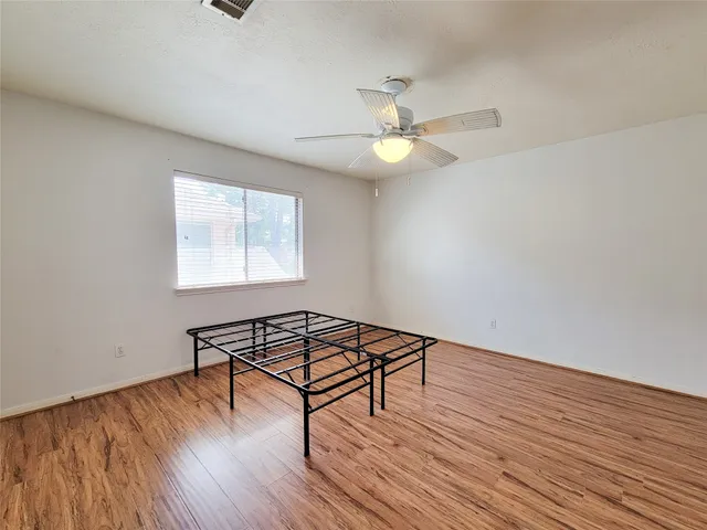 an empty room with wooden floor fan and windows