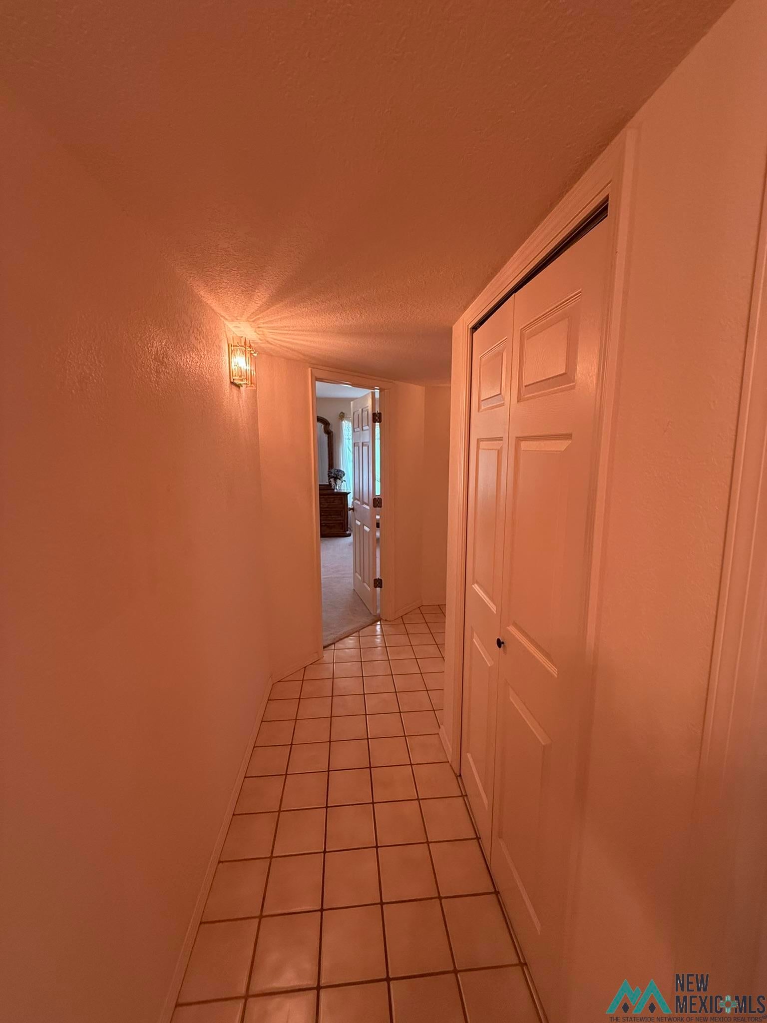 300 Rio Grande Circle Elephant Butte, NM 87935 - Photo 17 of 99 Tiled hallway featuring a wall-mounted light fixture, white bi-fold doors, and a doorway leading to an interior room