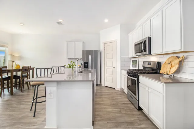 a kitchen with stainless steel appliances a microwave a stove a sink dishwasher a refrigerator with white cabinets and wooden floor