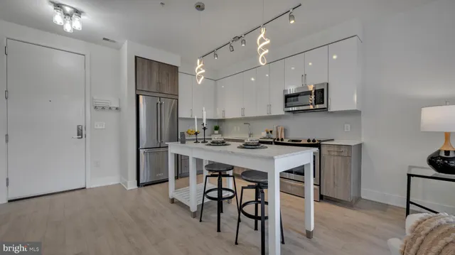 a kitchen with stainless steel appliances a refrigerator a stove a sink a dining table and chairs with wooden floor