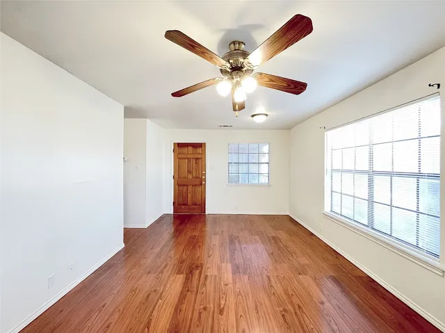 an empty room with wooden floor chandelier fan and windows