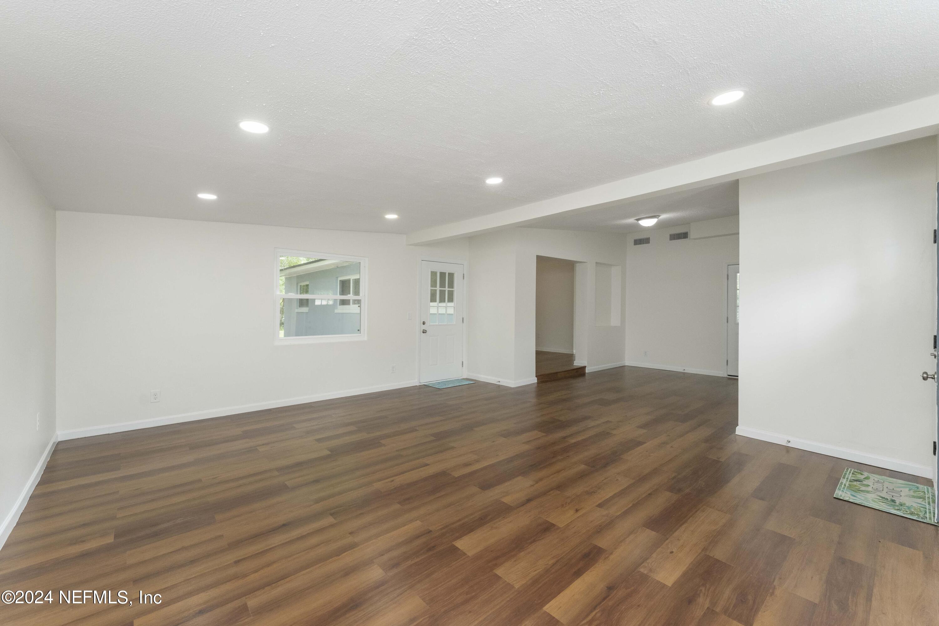 6937 Rollo Road Jacksonville, FL 32205 - Photo 5 of 26 an empty room with wooden floor and windows