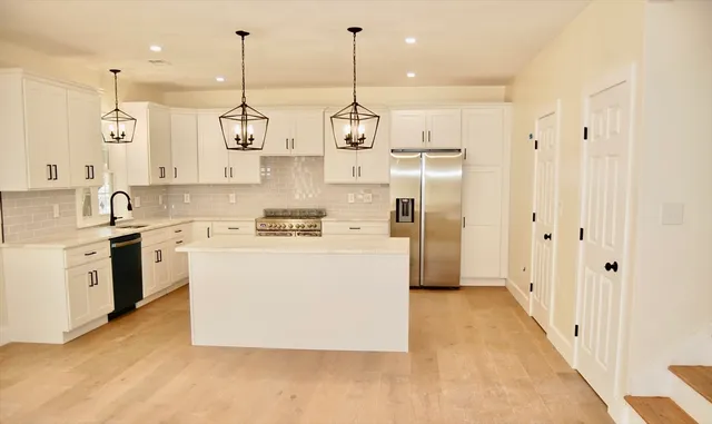 a kitchen with stainless steel appliances granite countertop a sink a stove a refrigerator and white cabinets