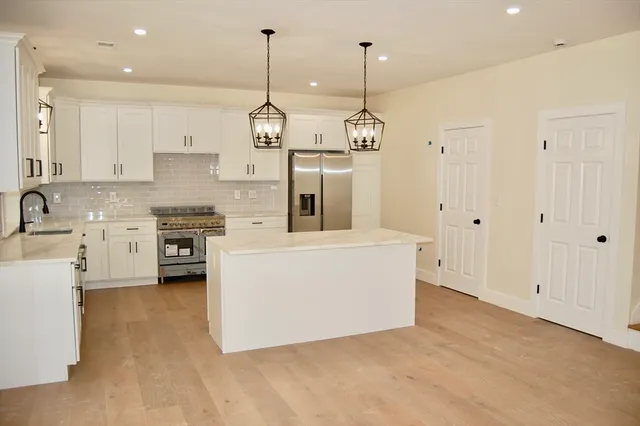 a large kitchen with stainless steel appliances granite countertop a stove a sink and white cabinets
