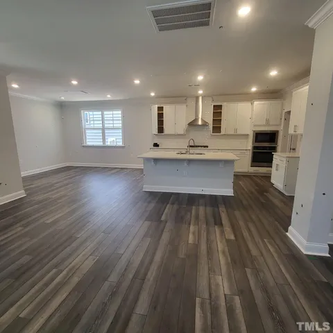 a large white kitchen with wooden floor and stainless steel appliances
