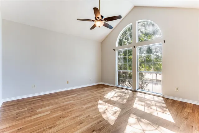 an empty room with wooden floor fan and windows