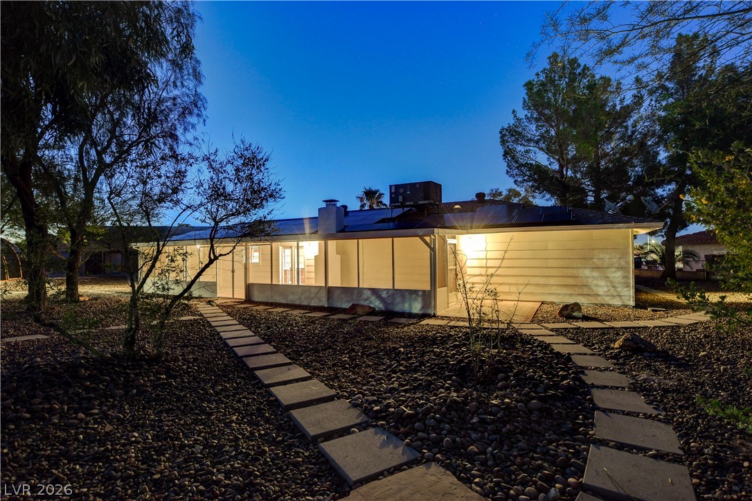 7631 Bermuda Road Las Vegas, NV 89123 - Photo 63 of 64 A flagstone path winds through rock landscaping toward a well-lit home under a twilight sky.