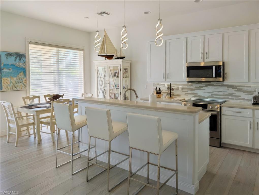 5758 Lago Villaggio Way Naples, FL 34104 - Photo 19 of 42 Kitchen with white cabinets, decorative light fixtures, stainless steel appliances, and an island with sink