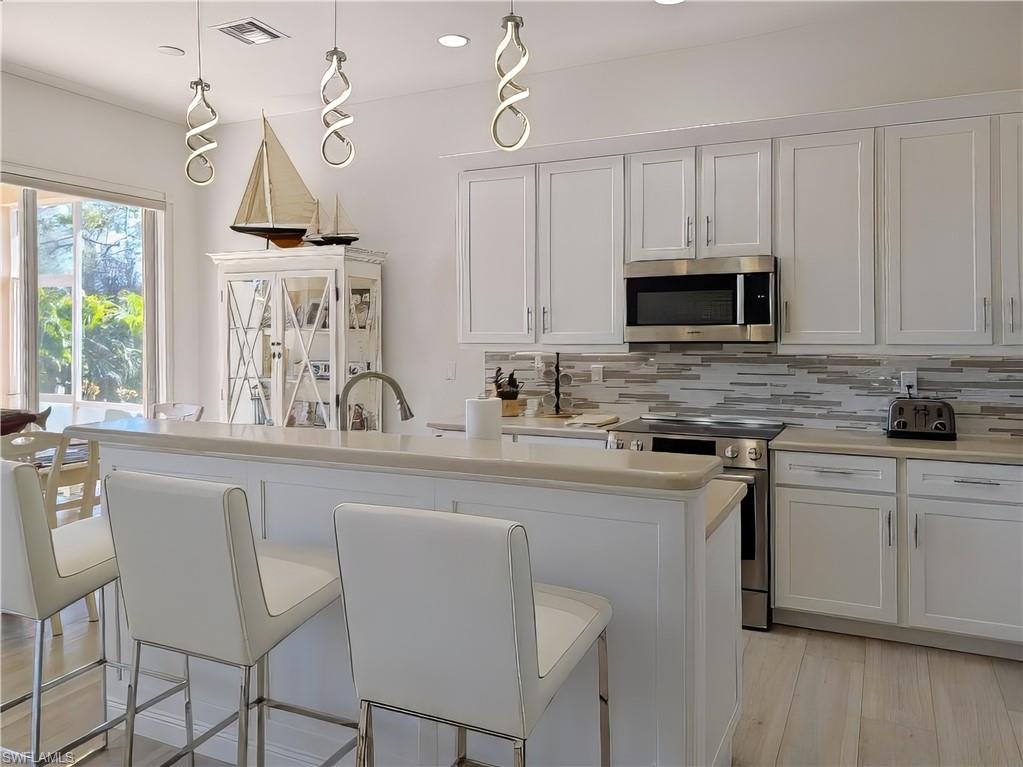 5758 Lago Villaggio Way Naples, FL 34104 - Photo 20 of 42 Kitchen with white cabinets, an island with sink, appliances with stainless steel finishes, decorative light fixtures, and a breakfast bar area