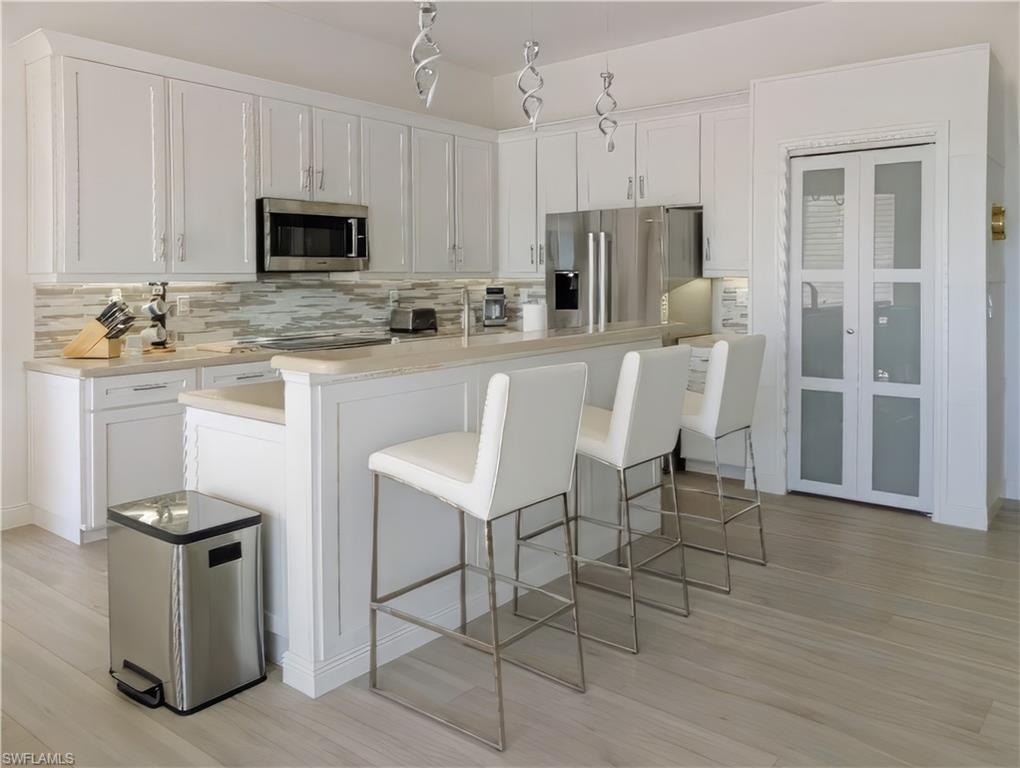 5758 Lago Villaggio Way Naples, FL 34104 - Photo 21 of 42 Kitchen featuring a kitchen breakfast bar, decorative backsplash, white cabinets, and stainless steel appliances