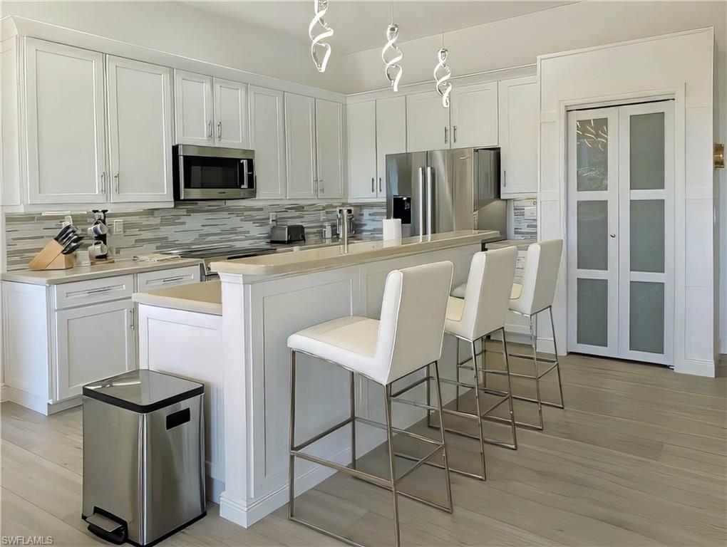 5758 Lago Villaggio Way Naples, FL 34104 - Photo 22 of 42 Kitchen with white cabinetry, decorative backsplash, a breakfast bar, a center island with sink, and appliances with stainless steel finishes