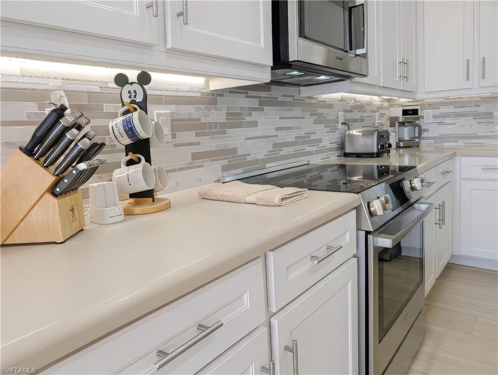 5758 Lago Villaggio Way Naples, FL 34104 - Photo 24 of 42 Kitchen featuring tasteful backsplash, white cabinetry, and stainless steel appliances