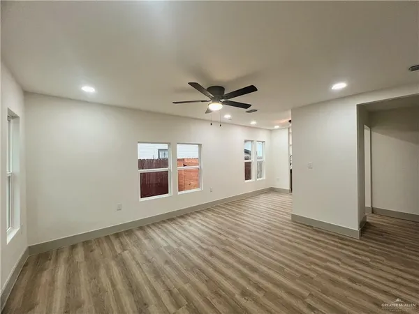an empty room with wooden floor a ceiling fan and windows