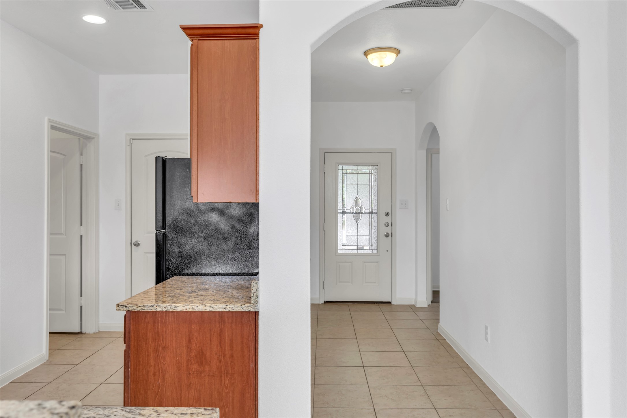 13213 Clara Martin Road Manor, TX 78653 - Photo 12 of 38 Kitchen featuring light tile patterned floors, light stone counters, arched walkways, wood finish cabinetry, and freestanding refrigerator
