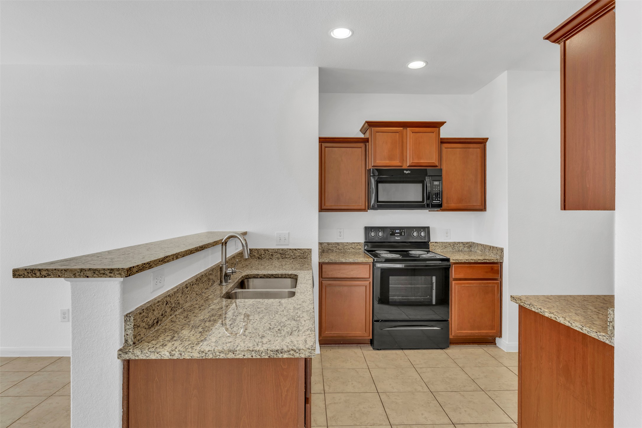 13213 Clara Martin Road Manor, TX 78653 - Photo 13 of 38 Kitchen featuring black appliances, wood finish cabinetry, light stone counters, a peninsula, and recessed lighting