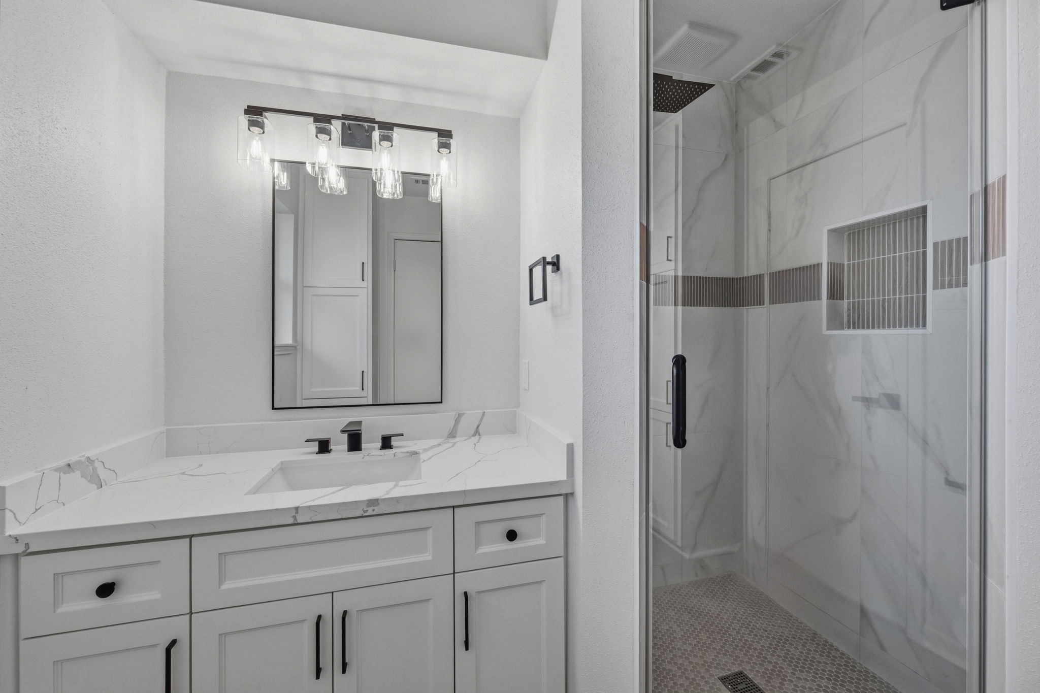 210 Ridgemont Drive Alvin, TX 77511 - Photo 23 of 27 This modern bathroom features a sleek vanity with a marble countertop and black fixtures. It includes a large mirror with stylish lighting above. The spacious tile shower has a glass door and contemporary design elements.