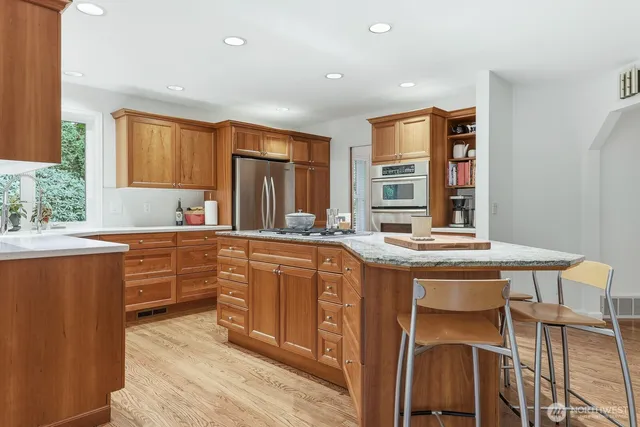 a kitchen with stainless steel appliances granite countertop a stove a sink dishwasher and a refrigerator with wooden cabinets