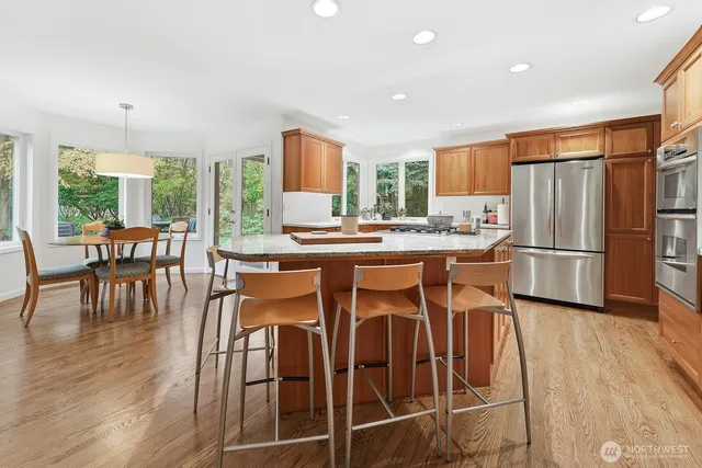 a kitchen with stainless steel appliances granite countertop a stove a refrigerator a dining table and chairs with wooden floor