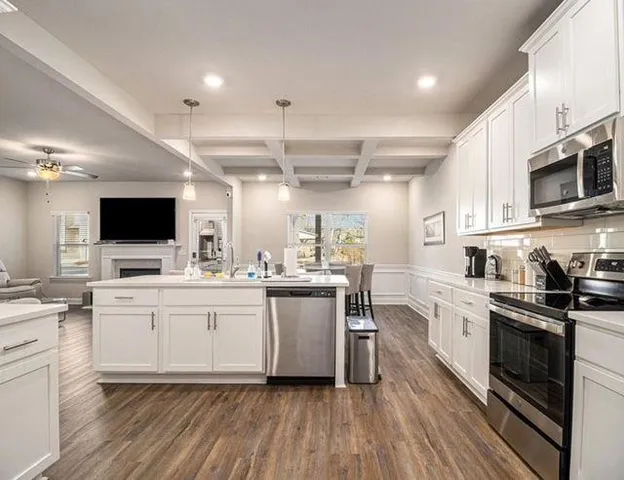 a kitchen with stainless steel appliances a white stove top oven a sink dishwasher and white cabinets with wooden floor