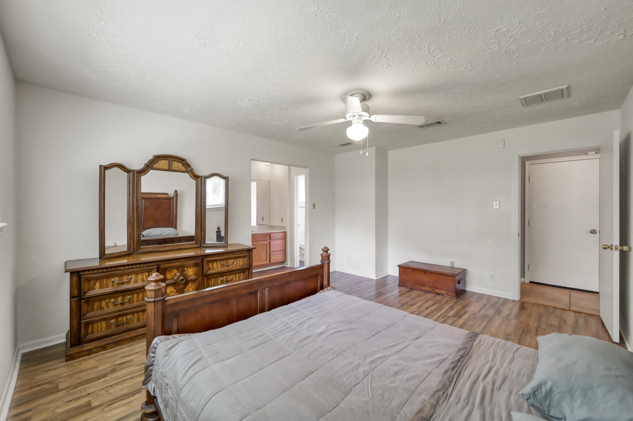 4314 Enchantedgate Drive Spring, TX 77373 - Photo 24 of 47 Spacious bedroom with hardwood floors, neutral walls, and a ceiling fan. Features a vintage wooden dresser with a large mirror and an adjoining bathroom.