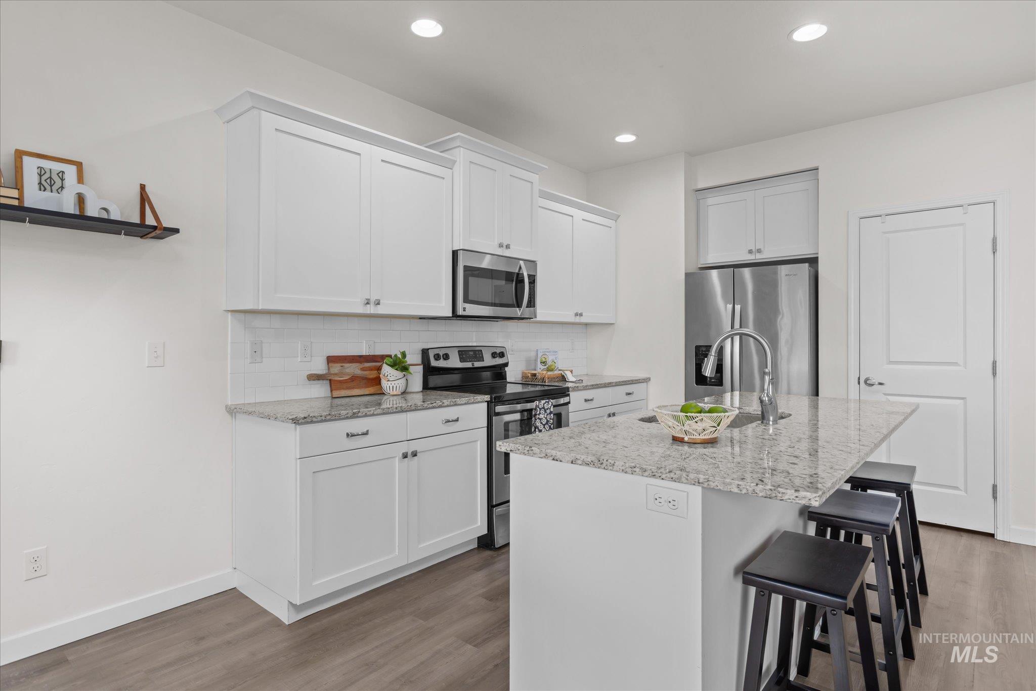 1885 North Justin Avenue Meridian, ID 83646 - Photo 11 of 27 Kitchen with stainless steel appliances, a breakfast bar, light stone countertops, a center island with sink, and light wood finished floors