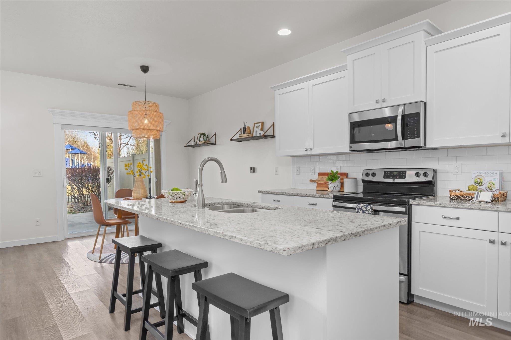 1885 North Justin Avenue Meridian, ID 83646 - Photo 15 of 27 Kitchen with stainless steel appliances, light wood finished floors, white cabinets, pendant lighting, and backsplash