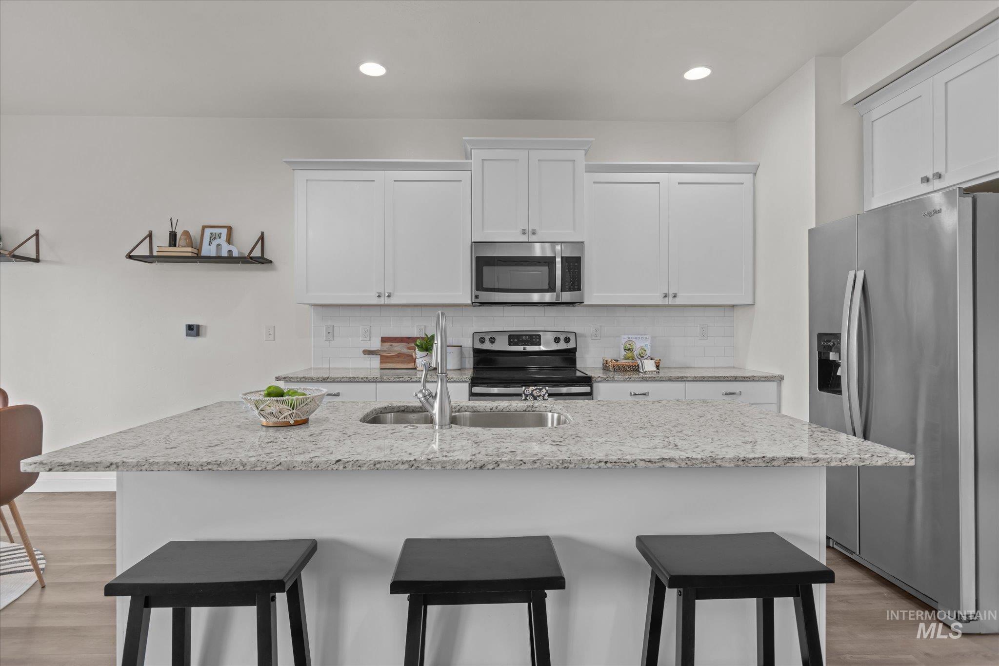 1885 North Justin Avenue Meridian, ID 83646 - Photo 21 of 27 Kitchen featuring a kitchen bar, light wood finished floors, stainless steel appliances, white cabinetry, and light stone counters