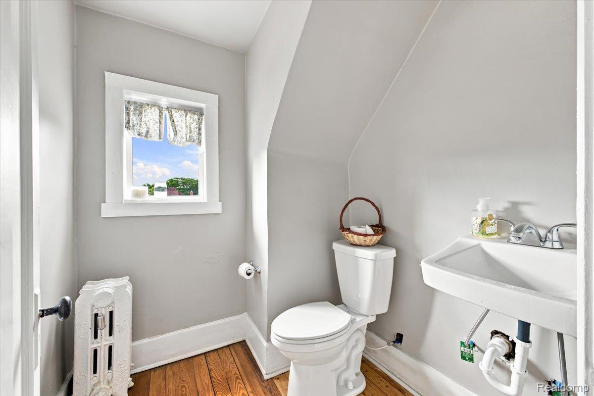 899 Edison Street Detroit, MI 48202 - Photo 29 of 37 Compact bathroom with wood-finish flooring, a wall-mounted sink, and a classic cast iron radiator