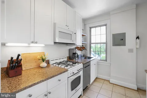 a kitchen with granite countertop a stove a sink and a white cabinets