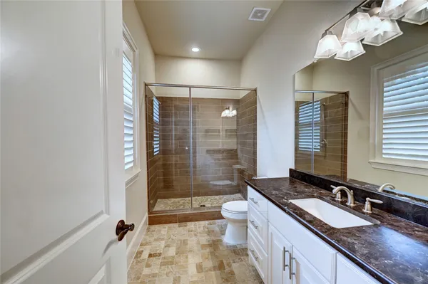a bathroom with a granite countertop sink a toilet a mirror and shower