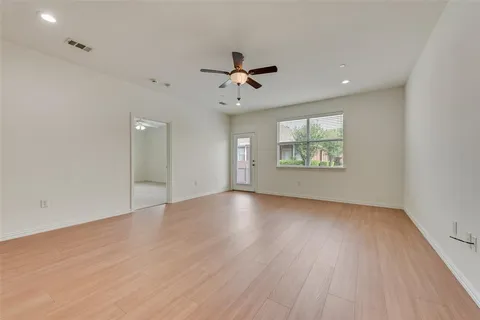 an empty room with wooden floor ceiling fan and windows