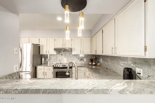 a kitchen with stainless steel appliances kitchen island granite countertop a refrigerator a stove a sink and white cabinets with wooden floor