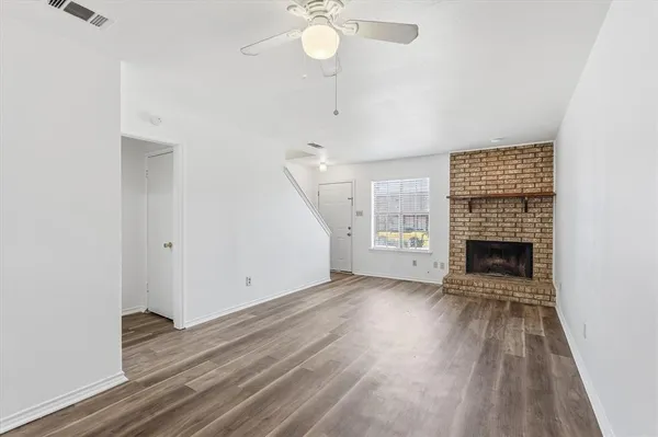 an empty room with wooden floor fireplace and windows