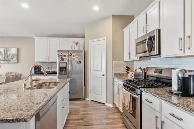 a kitchen with stainless steel appliances granite countertop a stove top oven a refrigerator a sink and dishwasher with white cabinets