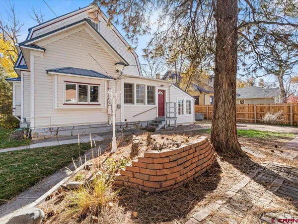 a view of a white house next to a yard with a large tree
