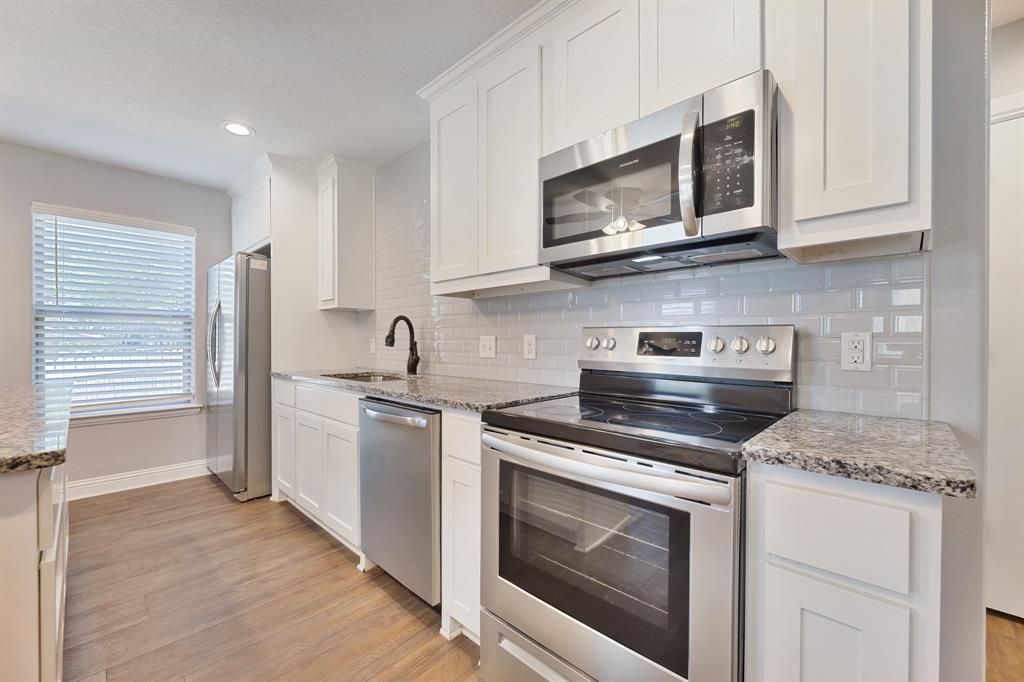 1713 Bronco Road Granbury, TX 76049 - Photo 9 of 23 Kitchen featuring stainless steel appliances, granite countertops, white cabinetry, a subway tile backsplash, and wood-finish flooring