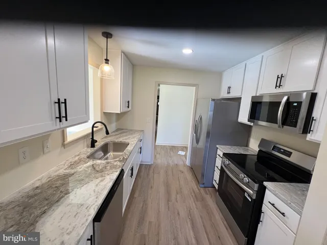 a kitchen with stainless steel appliances a sink dishwasher a refrigerator oven a sink with wooden floor and cabinets