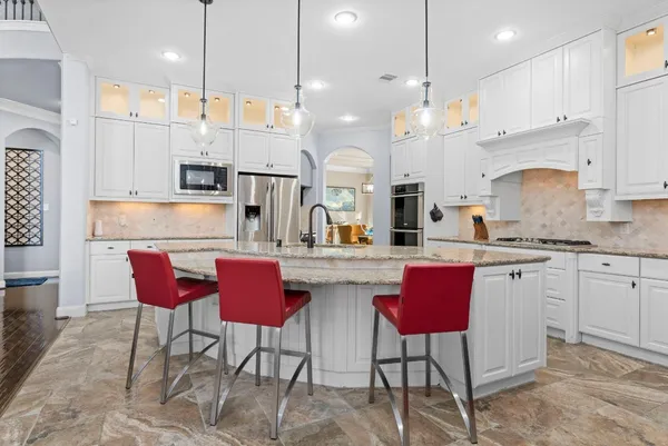 a kitchen with stainless steel appliances granite countertop a kitchen island a stove a sink a refrigerator a kitchen island with chairs and white cabinets