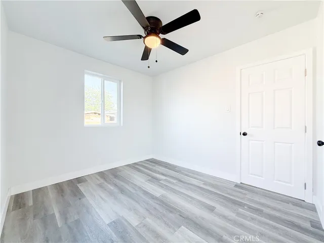 an empty room with wooden floor ceiling fan and windows