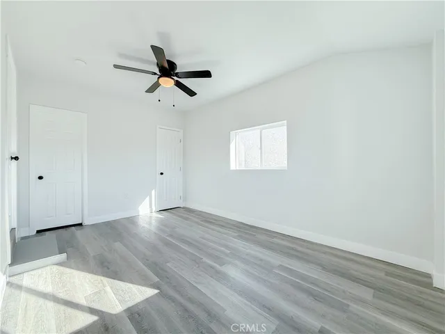an empty room with wooden floor ceiling fan and windows