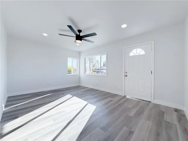 an empty room with wooden floor ceiling fan and windows