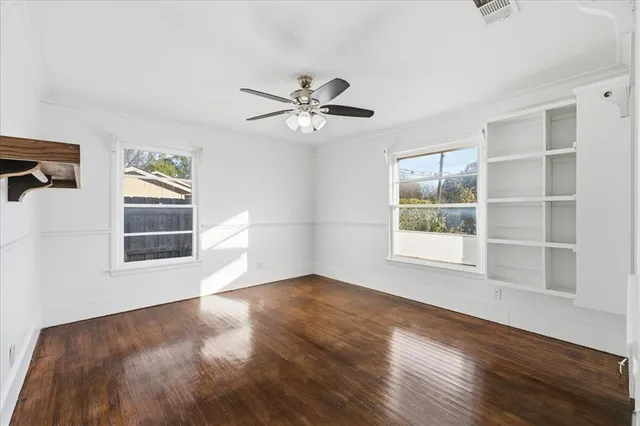 an empty room with wooden floor ceiling fan and windows