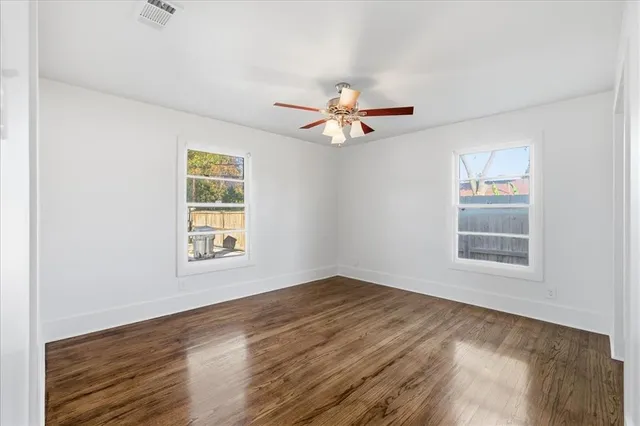 an empty room with wooden floor ceiling fan and window