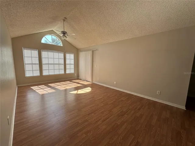 an empty room with wooden floor chandelier fan and windows