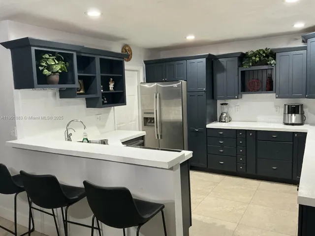 a kitchen with stainless steel appliances a sink a stove a refrigerator cabinets and chairs