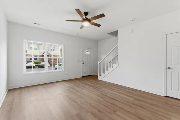 an empty room with wooden floor a ceiling fan and windows