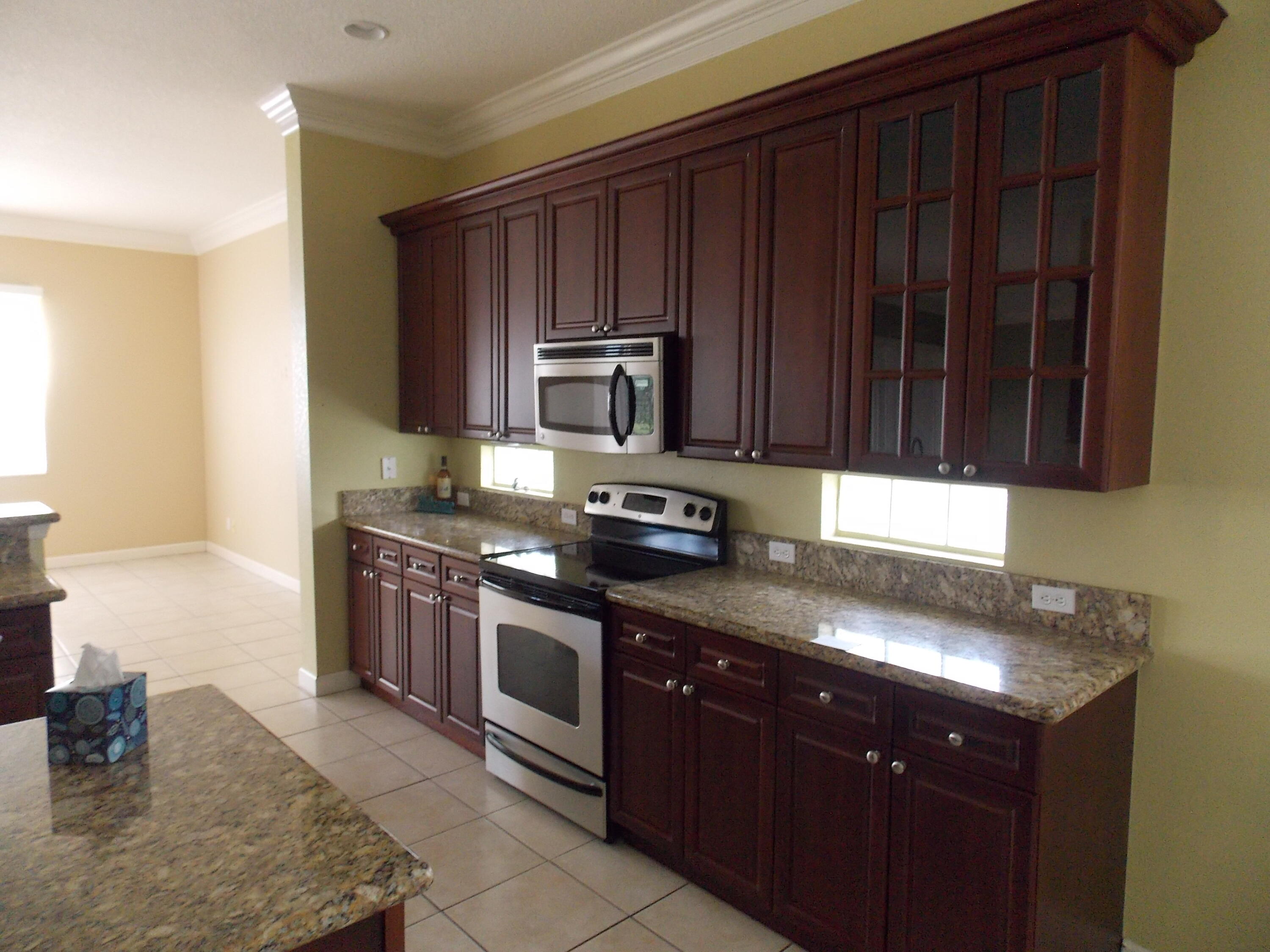 323 Northwest Sheffield Circle Port St. Lucie, FL 34983 - Photo 10 of 31 a kitchen with granite countertop wooden cabinets and a stove top oven